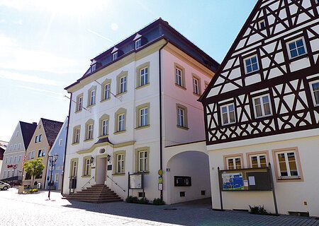Das Rathaus der Drei-Stämme-Stadt Monheim Straßenansicht der Monheimer Innenstadt: Im Vordergrund das Rathaus der Stadt Monheim, mit weiteren mehreren Gebäuden, darunter ein Fachwerkhaus, das man Schindlerhaus nennt.