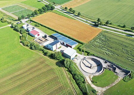 Städtische Kläranlage Monheim Luftaufnahme der städtische Kläranlage Monheim mit Solarpaneelen auf den Dächern, umgeben von grünen Feldern und Straßen.
