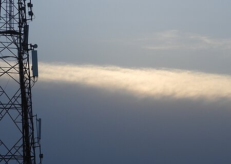 Mobilfunkmast Mobilfunk-Sendemast vor bewölktem Himmel mit einer schmalen, hellen Wolke im Hintergrund.