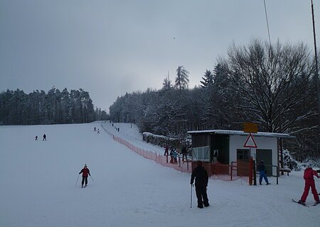 Schlepplift "Kaiserschachen" in Übersfeld Skifahrer auf einer schneebedeckten Piste neben einem kleinen Schlepplift und einem Wald im Hintergrund.