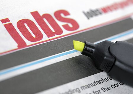 Stellenangebote Zeitungsseite mit dem Wort "Jobs" in großen roten Buchstaben und ein gelber Textmarker liegt auf der Zeitung.