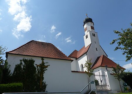 Filialkirche St. Michael Itzing Weiße Kirche mit rotem Ziegeldach und Zwiebelturm vor blauem Himmel. Im Vordergrund ein Tor und Pflanzen.