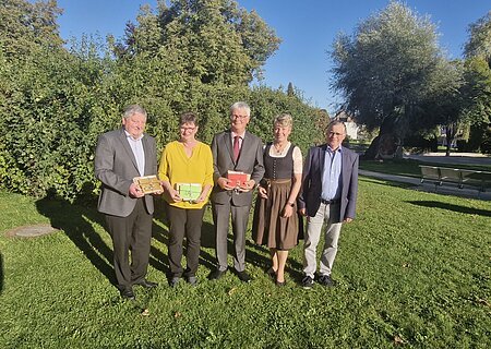 Verabschiedung Rentner 2025 Both Margit, Mayer Alfred, Josef Nuber Fünf Personen stehen auf einer Wiese vor Bäumen, drei halten bunte Geschenke in den Händen, im Hintergrund blauer Himmel. Renteneintritt der drei langjährigen Mitarbeiter der VG Monheim.