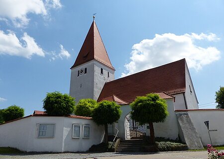 Pfarrkirche Mariä Himmelfahrt in Flotzheim Kirche mit rotem Dach, Turmuhr und umgebender weißer Mauer mit Eingangstor bei blauem Himmel und Bäumen davor.