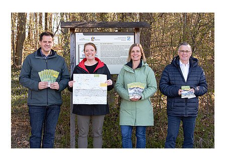 Wanderregion Monheimer Alb startet durch - v.l.n.r.: Peter Ferber (scheidender Geschäftsführer Erholungsgebiet Monheimer Alb e.V.), Silke Kronacher-Reilich (neue Geschäftsführerin Monheimer Alb), Melanie Pruis-Obel (Leader-Managerin), BGM Günther Pfeffere Vier Personen stehen lächelnd vor einer Informationstafel im Wald und halten Broschüren und eine Karte in den Händen.