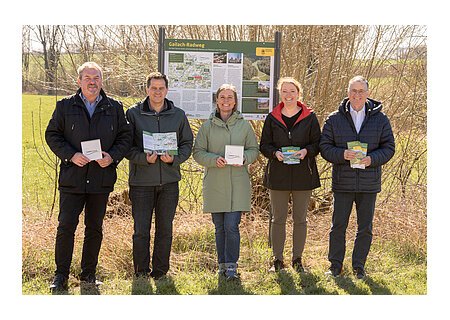 Gailach-Radweg offiziell eröffnet - v.l.n.r.: Bürgermeister Richard Mittl, StadtAktivManager Peter Ferber, Leader-Managerin Melanie Pruis-Obel, Geschäftsführerin Monheimer Alb Silke Kronacher-Reilich, Bürgermeister Günther Pfefferer Fünf Personen stehen lächelnd vor einer Informationstafel zum Gailach-Radweg in der Monheimer Alb und halten Broschüren und Schilder in der Hand, umgeben von grüner Wiese und Bäumen.