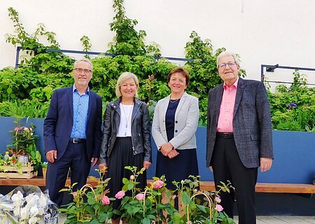 Verabschiedungsfeier der Verwaltungsgemeinschaft Monheim Vier Personen stehen vor einer bepflanzten Mauer mit Rosen und anderen Blumen im Vordergrund.