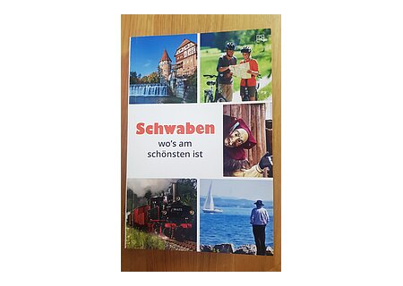 Reiseführer "Schwaben wo's am schönsten ist" Titelseite eines Reiseführers mit Fotos von einer Burg, Radfahrern, Fastnachtsmaske, Dampflok und Person am Seeufer. Titel in der Mitte "Schwaben wo's am schönsten ist".