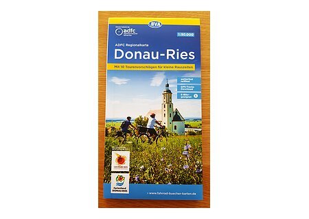 ADFC Radlkarte Neuauflage 2022 Cover der ADFC Regionalkarte Donau-Ries mit Radfahrern vor Kirche und Landschaft im Hintergrund. Unten links im Bild Logos vom Ferienland Donauries und des Geopark Ries.