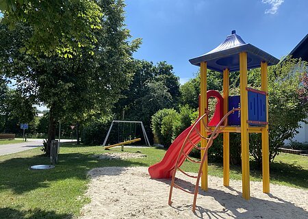 Spielplatz Habichtstraße Spielplatz mit Rutsche, Klettergerüst und Schaukel in einem Wohngebiet auf Gras- und Sandfläche bei Sonnenschein.