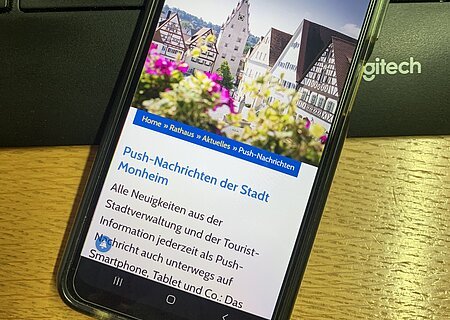 Push-Nachrichten der Stadt Monheim Schwarzes Smartphone zeigt Webseite der Stadt Monheim mit aufgerufener Seite zu Push-Nachrichten. Das Smartphone liegt auf der Tastatur und Holzoberfläche.