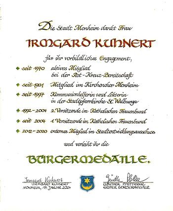 Irmgard Kuhnert Bürgermedaille Verleihung am 17. Januar 2024 Urkunde der Stadt Monheim für Irmgard Kuhnert mit Aufzählung der Tätigkeiten zu ihrem vorbildlichen Engagement und zur Verleihung der Bürgermedaille, darunter zwei Unterschriften und ein Wappen der Stadt Monheim. Datiert 17. Januar 2024.