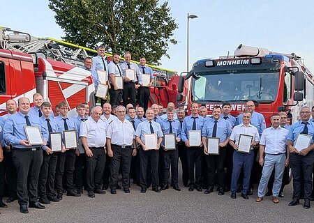 Alle Geehrten mit der „Fluthelfer-Nadel- und Urkunde“ am Abend der Feuerwehren in Monheim Gruppenfoto von Feuerwehrleuten in blauer Uniform in mehreren Reihen vor zwei roten Feuerwehrfahrzeugen, die meisten halten Urkunden, bei blauem Himmel.