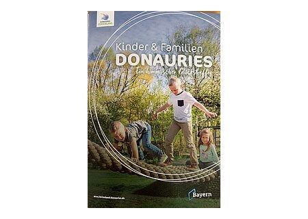 Broschüre Kinder & Familien DONAURIES Titelseite der Broschüre "Kinder & Familien Donauries" - Ein himmlischer Glückstreffer vom Ferienland Donau-Ries. Auf dem Titelbild drei Kinder spielend auf einem Kletterseil im Freien, umgeben von Bäumen und Wiese.