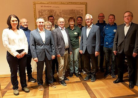 Spendenübergabe Sparkasse Nordschwaben Elf Personen stehen in einem Raum vor einer alten Landkarte an der Wand, teils in Anzügen, teils in Freizeitkleidung. Spendenübergabe der Sparkasse Nordschwaben an Monheimer Vereine und Verbände.