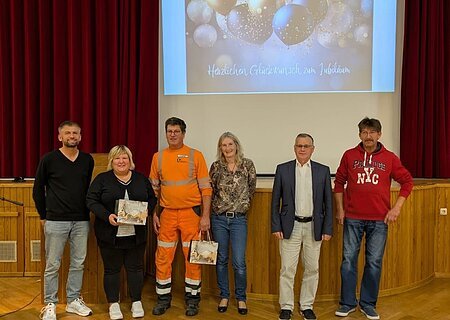 Personalrat - Jubilare 2025 Sechs Personen stehen nebeneinander auf einer Bühne vor rotem Vorhang und Leinwand mit Jubelbild und Text. Es handelt sich um den Personalrat der Stadt Monheim und geehrte Jubilare der Stadt Monheim.