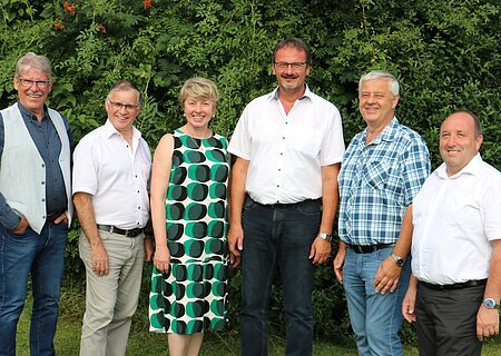 Verabschiedung Gerhard Leinfelder Sechs Personen stehen nebeneinander vor grünen Bäumen, alle blicken in die Kamera und lächeln.