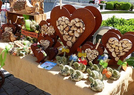 KunstHandWerkMarkt Monheim Handwerkskunst auf einem Marktstand: Herzförmige Holzdekorationen und Figuren aus Naturmaterialien auf einem Tisch.